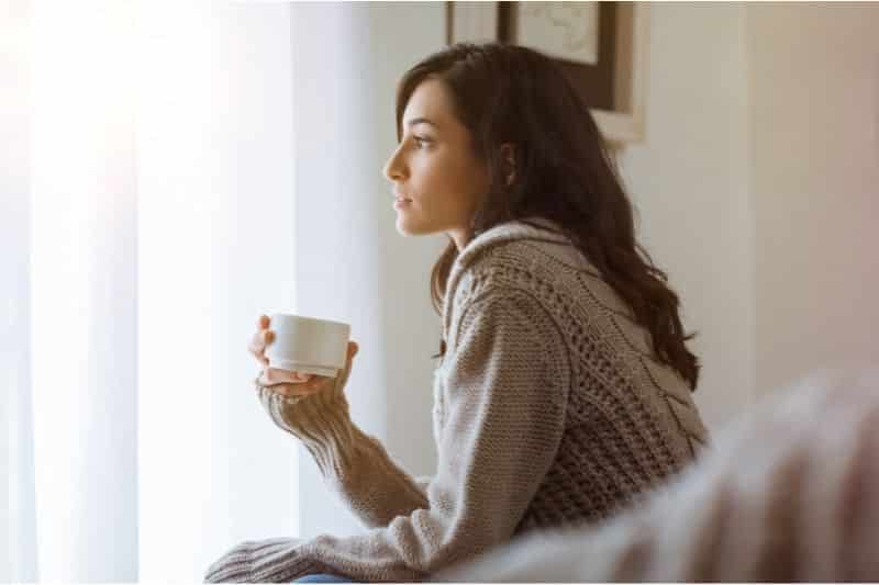 A woman sitting in front of a window holding a cup.